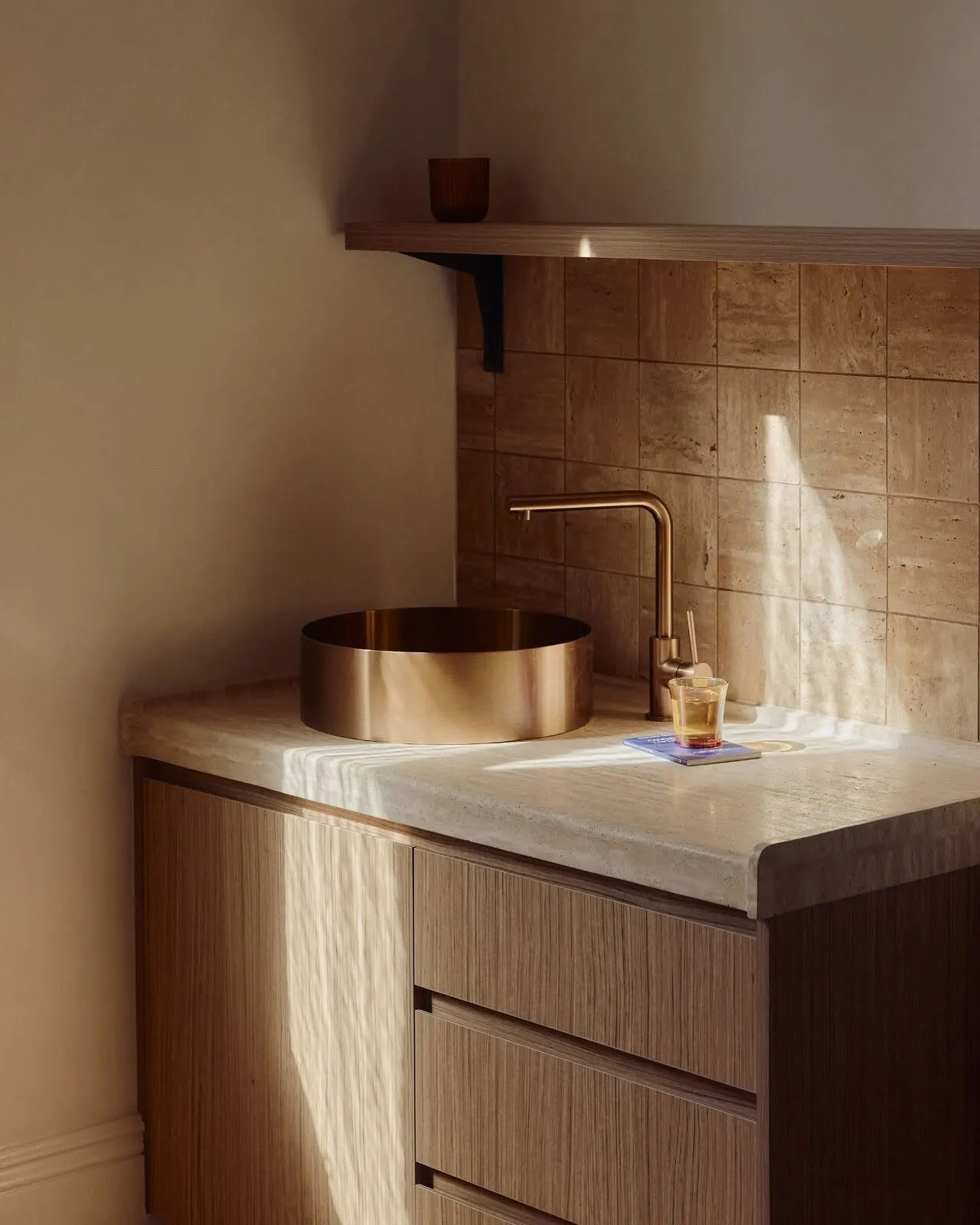 Afternoon light on a brass basin and travertine benchtop
