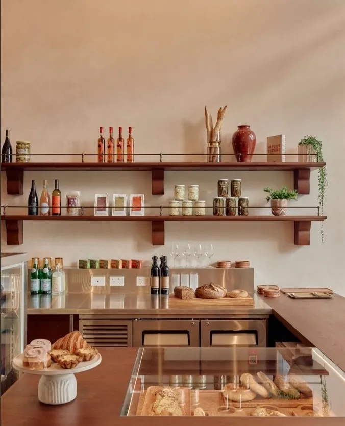 Timber shelves of bottles and jars above a counter of bread and pastries