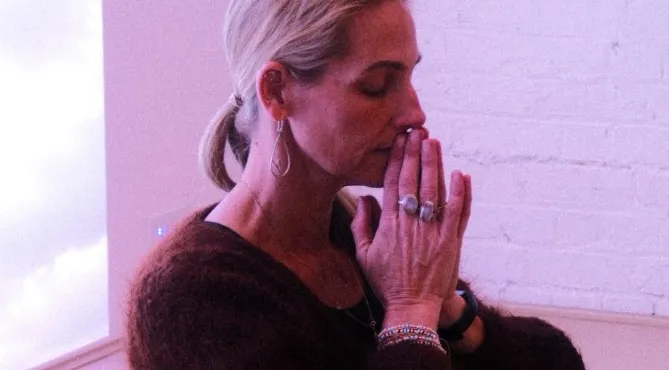 Donna seated in the studio with her hands together, eyes closed