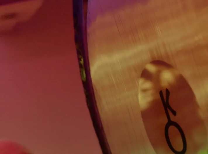 A felt mallet about to strike a large gong in warm light