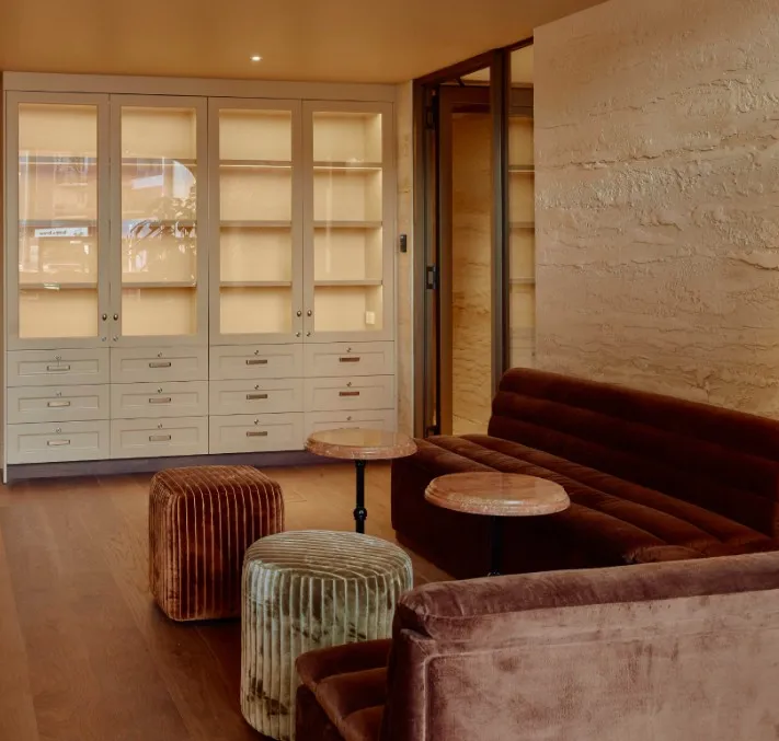 A lounge with velvet sofas, stools and a textured rammed-earth wall