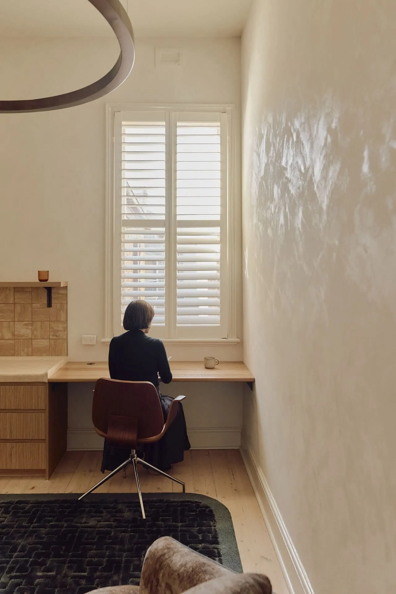 A practitioner at a timber desk beside a shuttered window